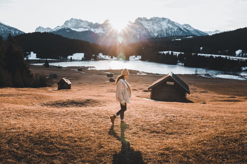 woman in brown coat standing on brown grass field near body of water